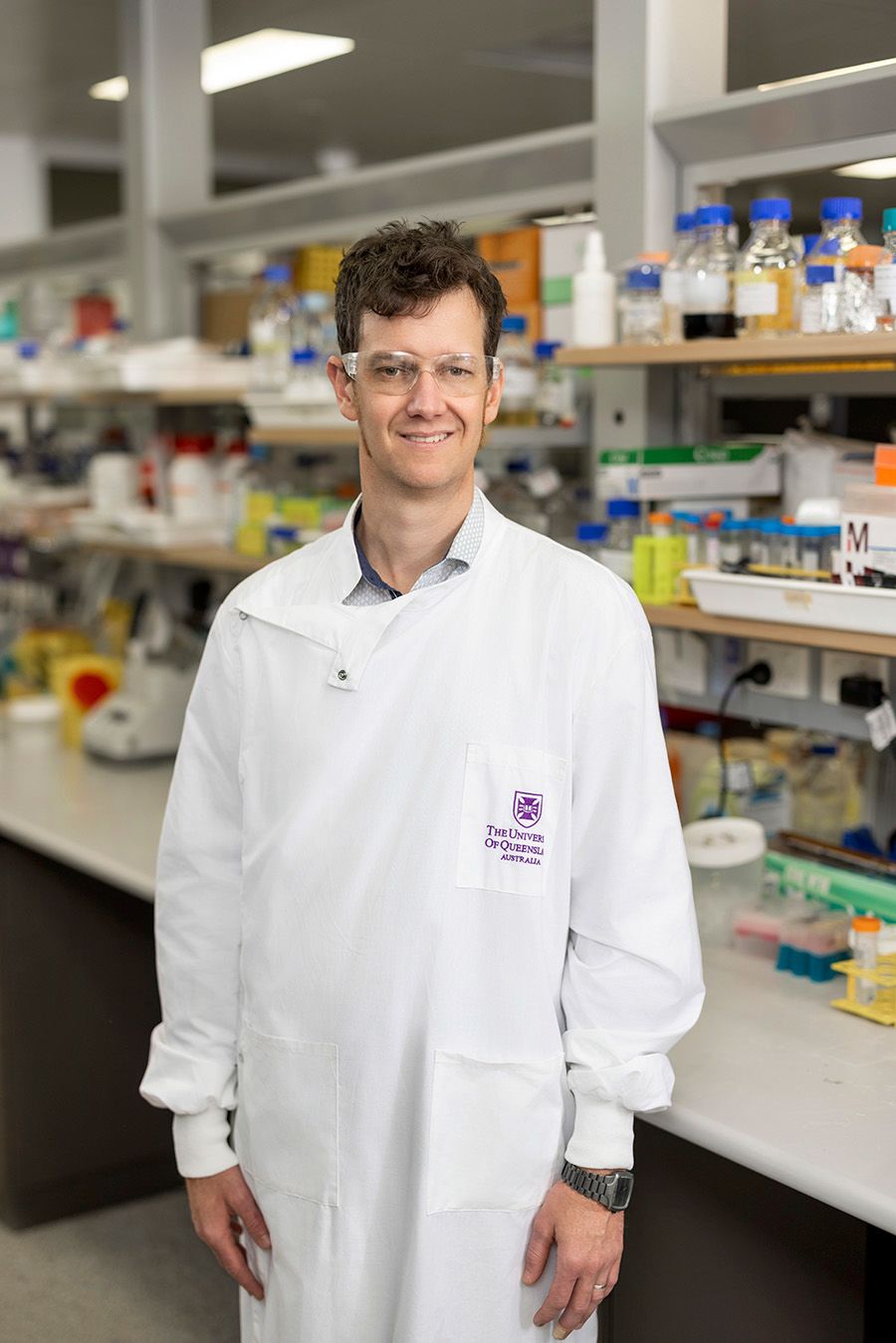 Associate Professor Keith Chappell standing in a lab wearing white coat with UQ logo