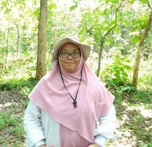 Arom Figyantika from Universitas Gadjah Mada (UGM), Indonesia is standing in the forest wearing a pink shawl and hijab under her broad-brimmed hat.