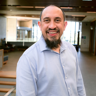 Ammar Abdul Aziz in a modern building at UQ St Lucia with a student seated behind him in the distance