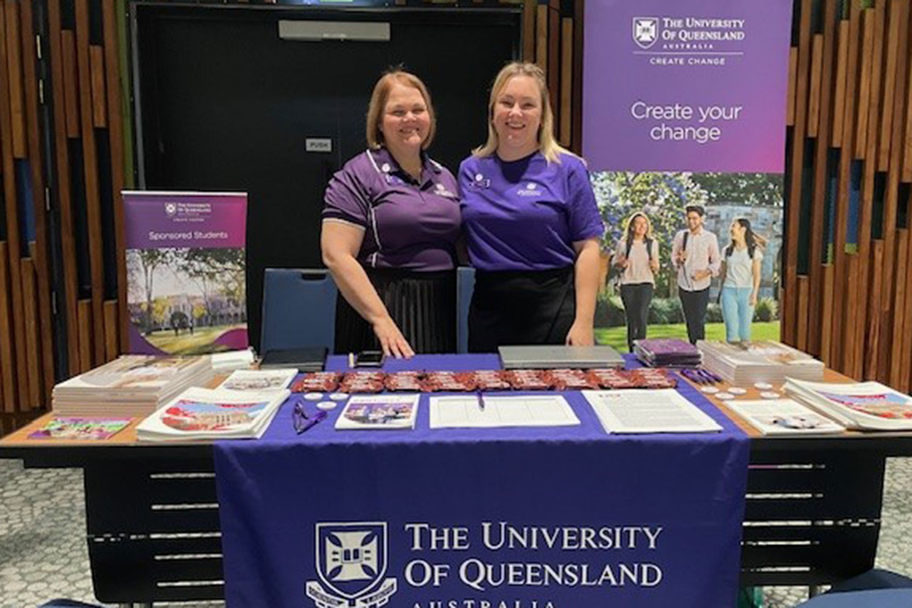 UQ's Rachel Panousis and Holly Peel standing in a Create Change stand wearing UQ-branded purple t-shirts