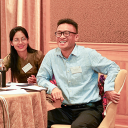 Thant laughing leaning on a table at the Australia Awards Myanmar conference