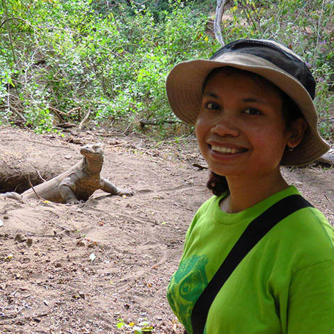 Maria Panggur standing at the Komodo National Park with a komodo dragon behind her.