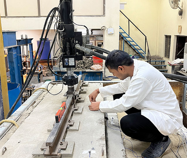 Harshal squats at a bench working with machinery behind him. 