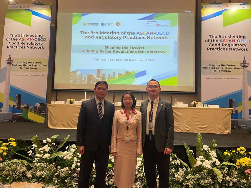 Khang Nguyen stands in front of a banner at the ASEAN-OECD 9th Conference with a man and a woman who are representing the government of Vietnam.