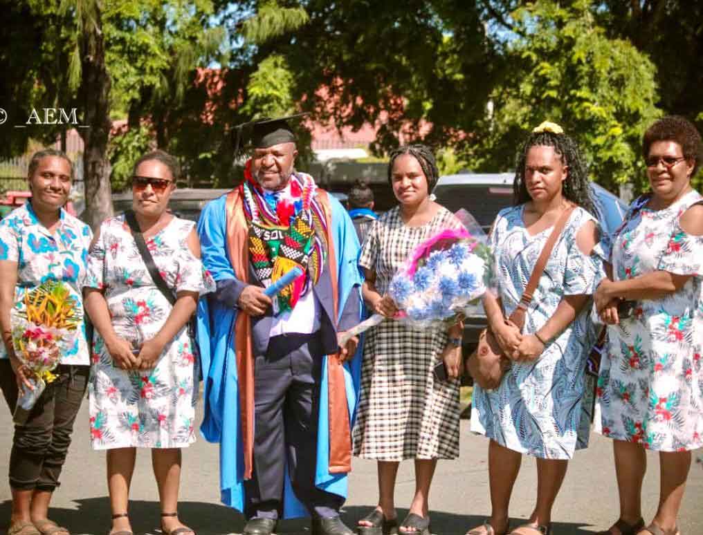Cedric stands between his wife and daughters at his masters graduation.