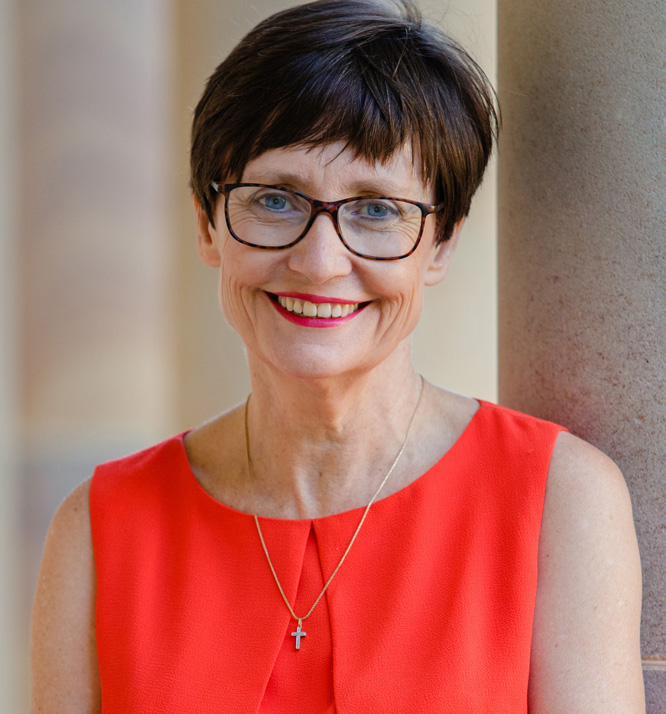 Rhonda Faragher wearing glasses smiling to camera with a short sleeve top - standing against sandstone columns