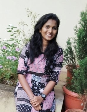 Abitha wearing a patterned dress beside pot plants and smiling sweetly.