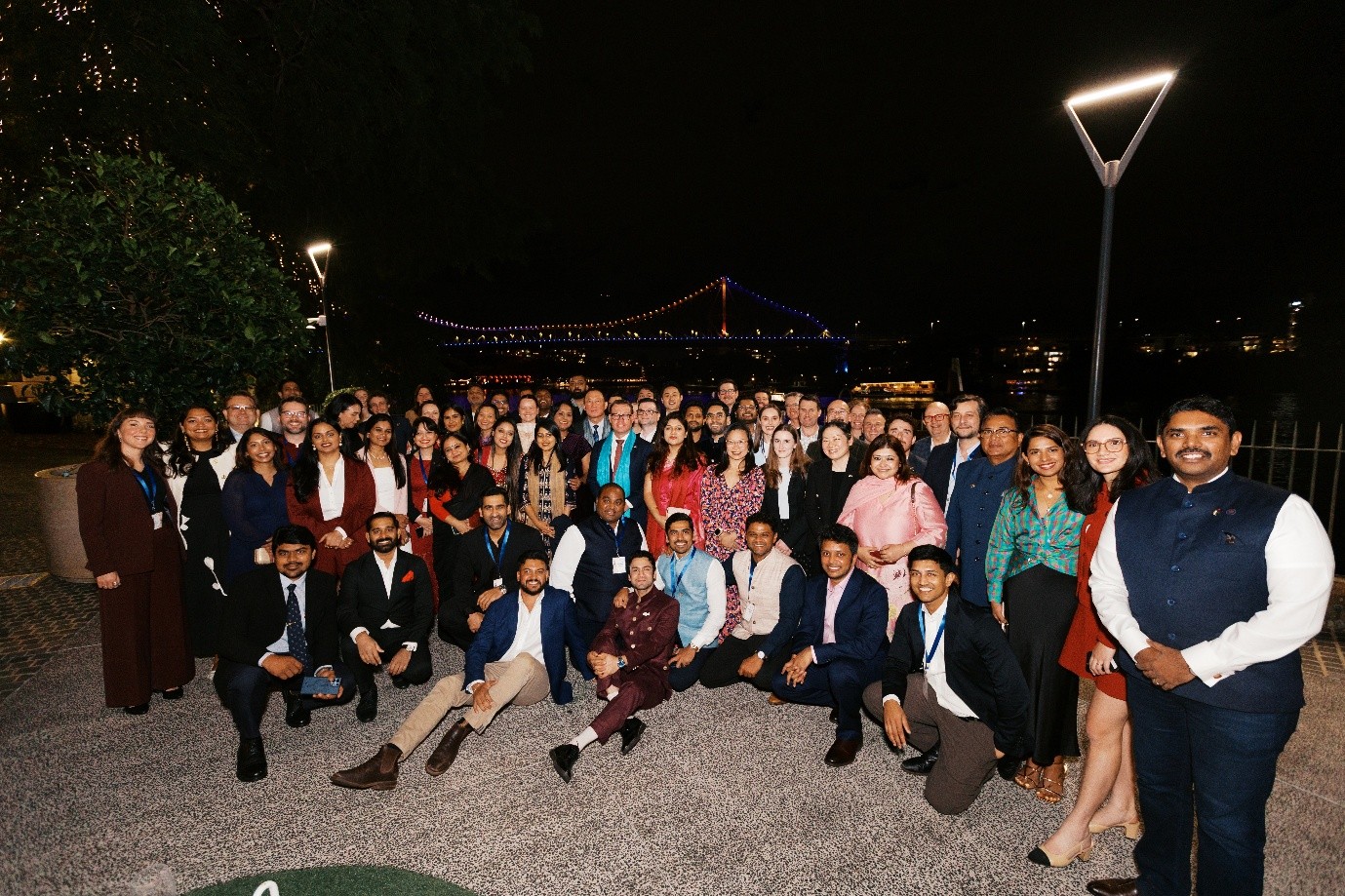 Group of Indian and Australian delegates alongside the Brisbane river at night with lights across the bridge