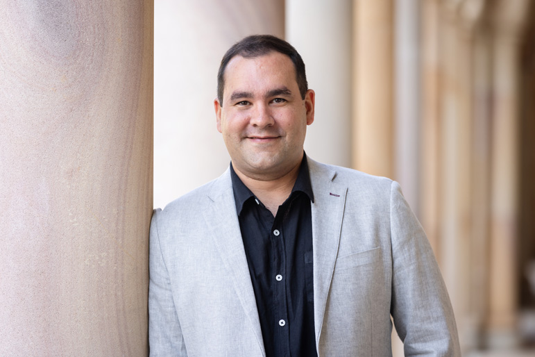 Edgar in a suit with shirt collar leaning against the Great Court's sandstone pillar