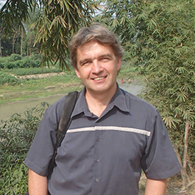 Dr Henning smiling with a jungle type forest behind him with green river