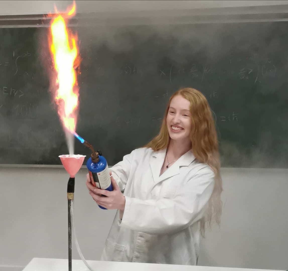 Science undergraduate, Emerald Gaydon, demonstrating a fire science experiment in front of a blackboard.