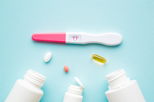three bottles open with pills out and a pregnancy test with double lines indicating a positive test