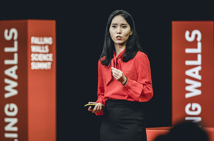 Dr Clara Jiang wearing a red shirt and speaking on stage at Falling Walls 2022.