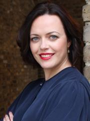 Claire leaning against brick wall looking to camera - wearing a formal and smart blouse