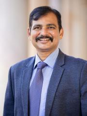 Saravanan Nagarathinam Saravanan in the Great Court UQ in front of sandstone pillars in a formal suit
