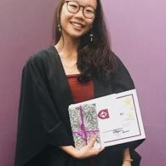 Hannah wearing a black graduation cloak, holding her testamur.