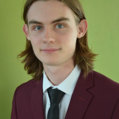 Max smiling without teeth to camera: green background, school uniform