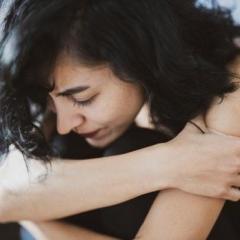 pale woman hugging her knees and looking down calmly
