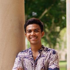Muhammad leaning against the Great Court's sandstone pillar in a long sleeved shirt and jeans. 