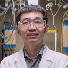 Dr Ma wearing lab glasses with machinery behind him with tubes running out of them. 