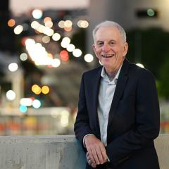 Professor Robert Henry leaning against a concrete railing with bright lights of traffic behind him