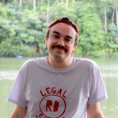 NCP Scholar Liam Lyttle looks at the camera with a river and densely forested river bank behind him. 