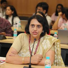 Dr Anita Gupta sitting at a desk with a microphone delivering the keynote speech.