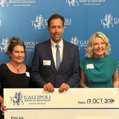 Nicholas Gilson from UQ standing with two female colleagues holding a cheque that reads Gallipoli Medical Research pay to Health and Wellbeing Centre for Research Innovation, UQ $250,000