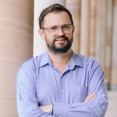 Ben smiling and standing in front of sandtone columns in UQ's Great Court