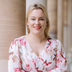 Holly smiling and standing in front of sandtone columns in UQ's Great Court