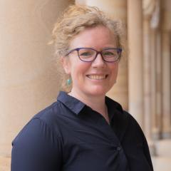 Jenny Dunn wearing glasses and standing against sandstone column