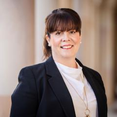 Kelly Vink wearing a suit jacket and blouse, full fringe - in front of the Great Court sandstone pillars