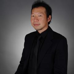 Jun Yan Change photographed in formal black shirt in indoor formal setting. 