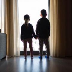 two children holding hands looking out a window. You see their silhouettes. 
