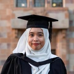 Nur Aneesa in her full graduation gown standing in the Great Court with a sandstone building behind her. 
