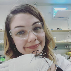 Samantha in the lab with a golden orb weaving spider walking over her gloved hand. 