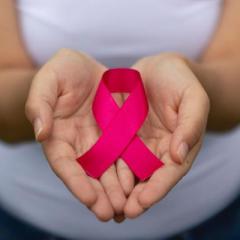 Woman holding pink ribbon folded in iconic image of breast cancer survivorship