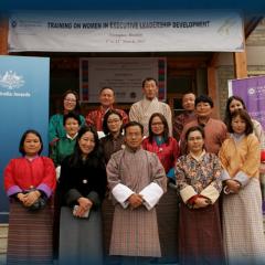 Bhutan WELD participants in traditional dress on steps with banners either side of Australia Awards and UQ International Developement
