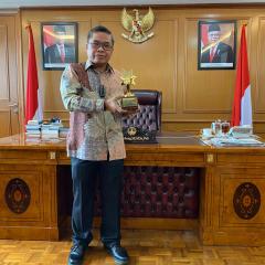 Dr Alue Dohong holding his award in front of office desk