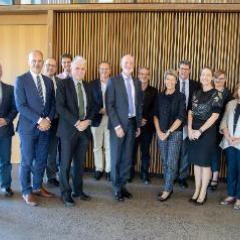 Ambassadors and UQ staff standing in front of slatted wooden wall - inside - dressed formally. 