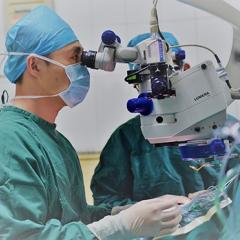 Doctors in full surgical gown gear looking through microscope
