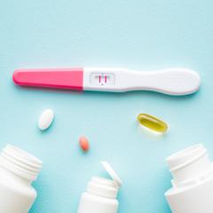 three bottles open with pills out and a pregnancy test with double lines indicating a positive test