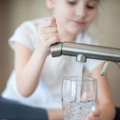 child filling up glass of water from tap 
