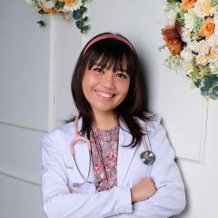 Dr Lady in lab coat with stethoscope around neck leaning against a wall with flowers hanging down