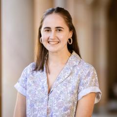 Arielle wears a floral blouse with hair down standing in front of sandstone pillars in the University of Queensland's Great Court