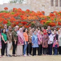 Australia Awards participants gathered as one group standing in front of a flame red tree on the grounds of the Great Court, St Lucia UQ 